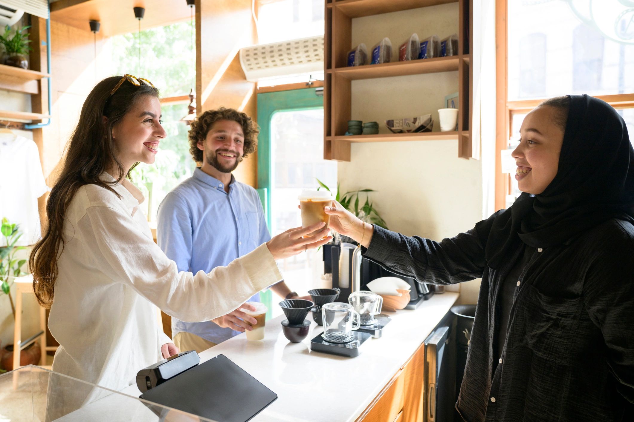 Smiling female barista serving iced coffee to happy customers in coffee shop