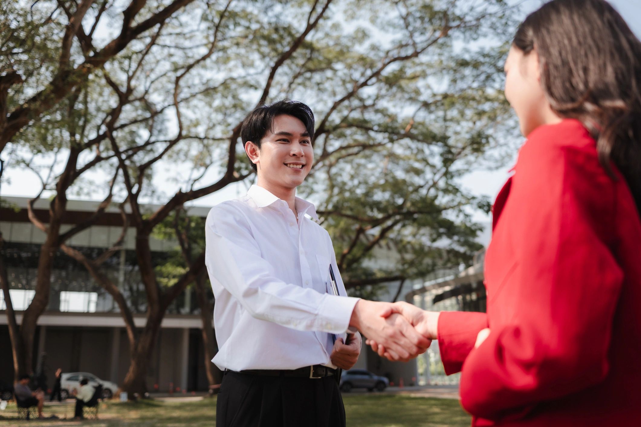 Smiling young man and woman shaking hands outdoors in casual clothes